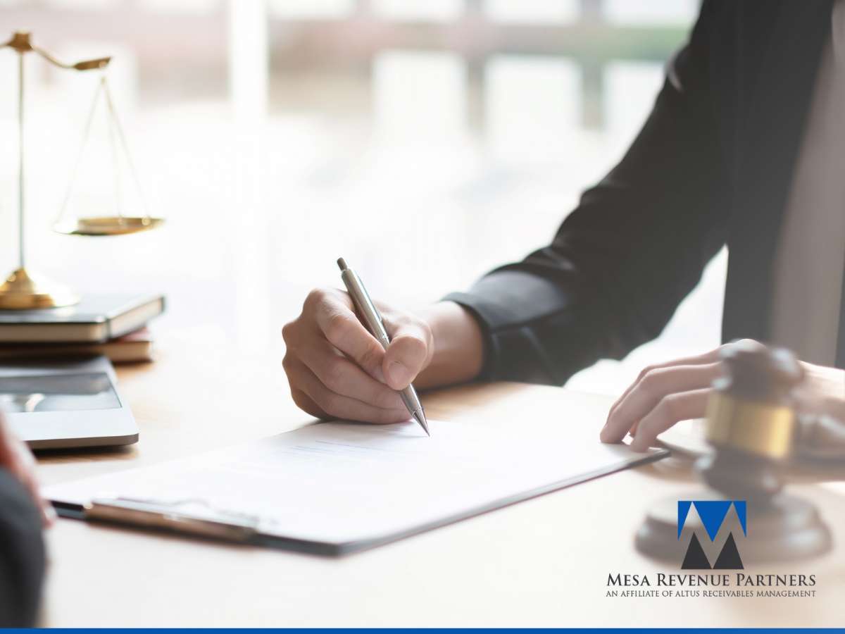 Businessperson signing a document at a desk, symbolizing clear communication of Payment Expectations, with legal and financial tools nearby, representing Mesa Revenue Partners